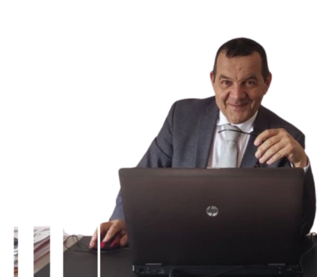 “Una persona seduta alla scrivania utilizza un computer portatile. Indossa un abbigliamento formale e guarda verso la camera con espressione cordiale. Sul tavolo sono presenti documenti e un mouse, a rappresentare un contesto di lavoro professionale.”